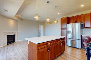 A kitchen island with cherry-stained wooden cabinets and a light quartz countertop, in front of a spacious living room with a fireplace.