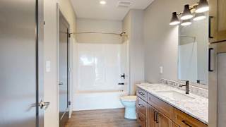 Modern apartment bathroom with a single-sink vanity, wood cabinetry, stone-look countertop, large mirror, bathtub and shower combination, and neutral finishes.