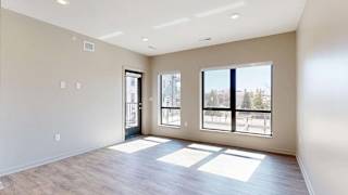 Bright open-concept apartment living area with wood-style flooring, large windows, abundant natural light, and a glass door leading to a private balcony.