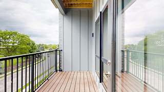 Private apartment balcony with wood decking, black metal railing, and treetop views.
