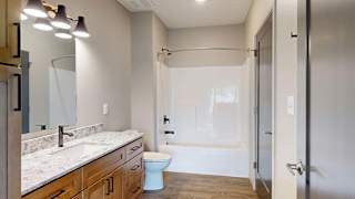 Modern apartment bathroom with a tub and shower, single-sink vanity, and wood cabinetry.