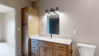 Modern apartment bathroom with a single-sink vanity, wood cabinetry, and a large mirror.