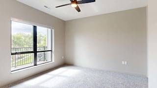 A room with a ceiling fan and a large window overlooking a balcony.