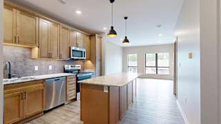 Modern apartment kitchen with a large island, wood cabinetry, and stainless steel appliances.
