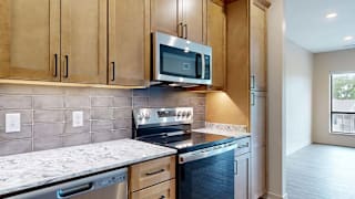 Modern apartment kitchen with wood cabinetry, stainless steel appliances, and a tile backsplash.