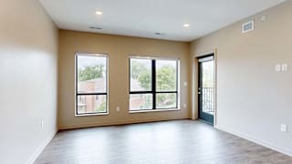 Bright apartment living area with wood-style flooring, large windows, and a door leading to a private balcony.