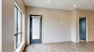 Bright apartment living area with wood-style flooring, large windows, and a door leading to a private balcony.
