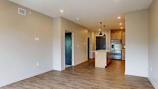Open-concept apartment living area with wood-style flooring and a kitchen with an island.