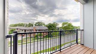Private apartment balcony with black metal railing and views of neighboring homes and trees.