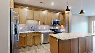 Open-concept apartment kitchen featuring a center island, warm wood cabinets, stainless steel appliances, and pendant lighting overlooking the living area.