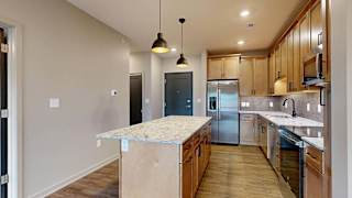 Spacious apartment kitchen with an oversized island, tile backsplash, wood cabinetry, and stainless steel appliances in a bright open layout.