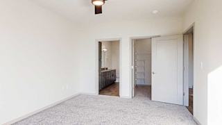 a bedroom with a carpeted floor, a ceiling fan, an attached bathroom, and a spacious walk-in closet