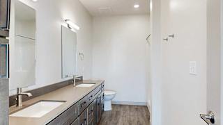 a bathroom with a quartz double vanity sink, a mirror with overhead lighting, and a walk-in shower