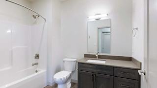 a bathroom with a quartz vanity sink, a mirror with overhead lighting, and a combination shower and tub
