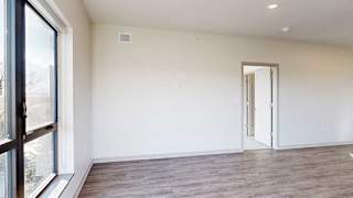 a living room with a large window, hardwood flooring, and a door to a bedroom