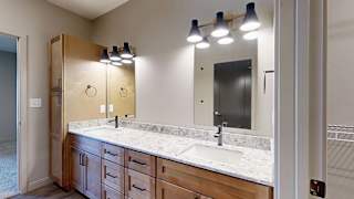 Modern apartment bathroom with a double-sink vanity, wood cabinetry, quartz-style countertop, large mirror, and contemporary wall-mounted lighting.