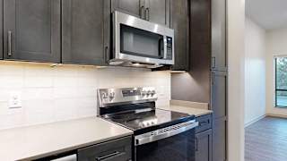 a kitchen with dark wooden cabinets, tile backsplash, quartz countertops, and a stainless steel microwave and oven