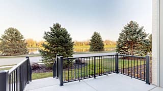 a black metal railing of a patio in front of trees and a pond