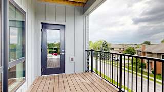 A balcony with a black metal railing, a windowed door to the living room, and a view of the neighborhood.