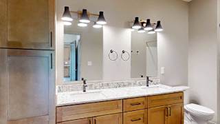 A bathroom with warm wooden cabinets, a quartz double vanity sink, two mirrors with overhead lighting, and tall storage cabinet.