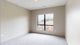 A bedroom with a large floor-to-ceiling window, and carpeted flooring.