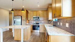 A kitchen with warm wooden cabinets, quartz countertops, a central island, and stainless steel appliances.