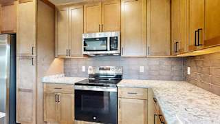 A close up of the stainless steel microwave and range in a kitchen with warm wooden cabinets.