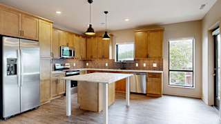 A kitchen with warm wooden cabinets, quartz countertops, a central island, and stainless steel appliances.