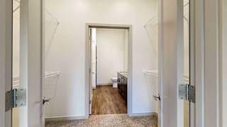 a closet with built-in shelving and hanging space that connects the primary bedroom to the primary bathroom