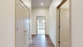 a hallway with an open door on the right, a closet double door on the left, and a bedroom at the end of the hall