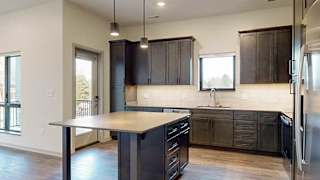 a kitchen with dark wood cabinets, a large kitchen island table, stainless steel appliances, and light quarts countertops