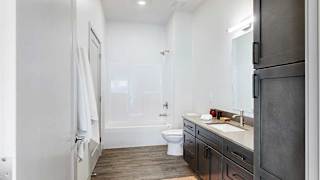 A walk-through bathroom with a wide quartz vanity and a white tub shower.