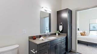 A bathroom with a quartz vanity, dark wooden cabinets, a tall storage cabinet, and a door open to a bedroom.