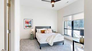 A furnished bedroom with a bed, modern art, a ceiling fan, and a floor-to-ceiling window.