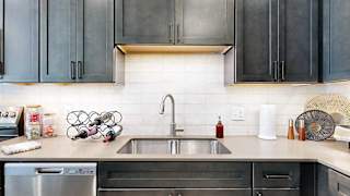 A modern kitchen sink with quartz counters, dark wooden cabinets, and a tile backsplash.