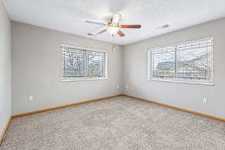 Apartment bedroom with carpet flooring, ceiling fan, and natural light.