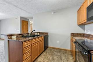 Kitchen featuring granite peninsula counter, wood cabinets, and black appliances.