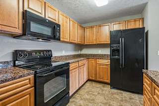 Updated kitchen with wood cabinetry, granite countertops, and black appliances.