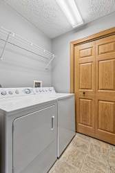 In-unit laundry room with washer, dryer, overhead shelving, and tile flooring.