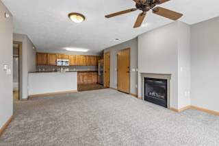 Open-concept living space with carpet flooring, fireplace, and kitchen view.