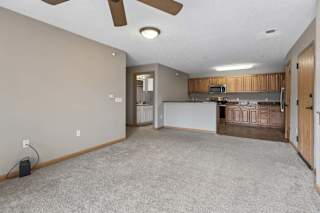 Open living area with carpeted floors, ceiling fan, breakfast bar, and adjacent kitchen.