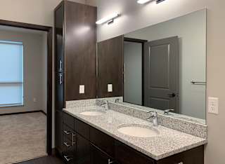 bathroom with dual sinks and dark brown cabinets and storage closet