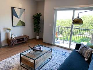 Spacious furnished living room with hard wood style flooring and scenic view of tree line in Lincoln at Haven at Uptown.
