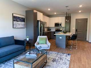 Furnished open concept living room looking into large kitchen in Bliss floor plan at Haven at Uptown in Lincoln.