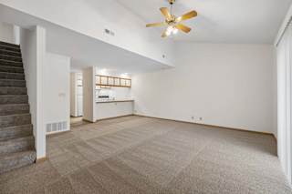 Open living room with vaulted ceiling and ceiling fan, carpeted staircase, and a breakfast bar connecting to the kitchen.