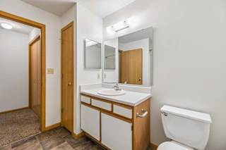 Apartment bathroom with a single-sink vanity, large wall mirror, toilet, and neutral finishes, with the hallway and bedroom visible through the open doorway.