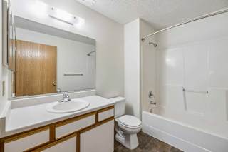 Apartment bathroom with a single-sink vanity, large wall mirror, toilet, and a tub/shower combination with built-in shelving in a bright, neutral interior.