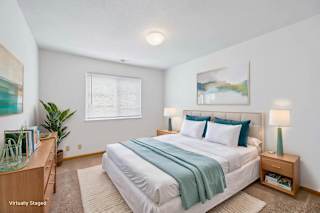 Virtually staged bedroom with a large bed, bedside lamps, window, artwork, and wood-look flooring in a bright interior.