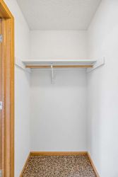 Apartment closet with a single hanging rod, upper shelf, neutral walls, and carpeted flooring for convenient storage.