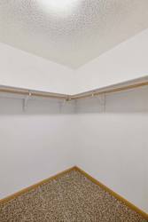 Walk-in apartment closet with wraparound hanging rods, upper shelving, neutral walls, and carpeted flooring for organized storage.